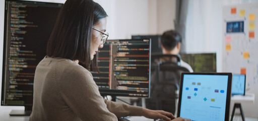 Young adult Asian male, female software developer coding program on desktop computer. Man, woman...