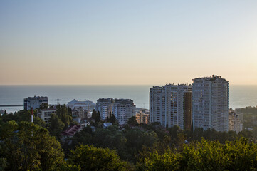 Fototapeta premium Panoramic top view of the evening city of Sochi with a beautiful sunset and buildings blurred in the haze among the trees