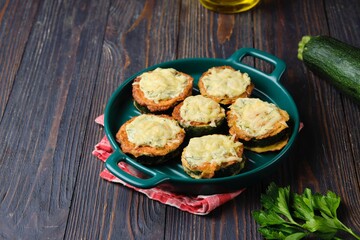 Zucchini stuffed with minced chicken and baked with cheese and herbs in a green baking dish on a dark wooden background.