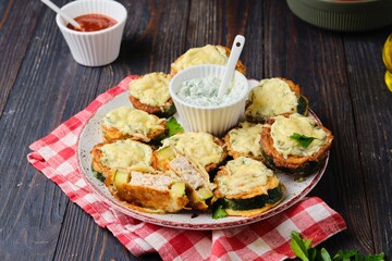 Zucchini stuffed with minced chicken and baked with cheese and herbs on a ceramic plate on a dark wooden background. Zucchini recipes.