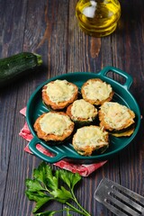 Zucchini stuffed with minced chicken and baked with cheese and herbs in a green baking dish on a dark wooden background.