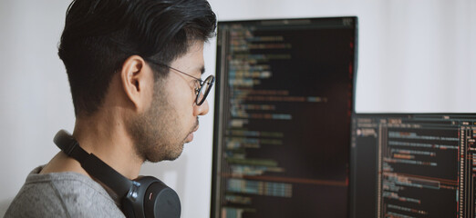 Young adult Asian male software developer coding program on desktop computer. Man work from home,...