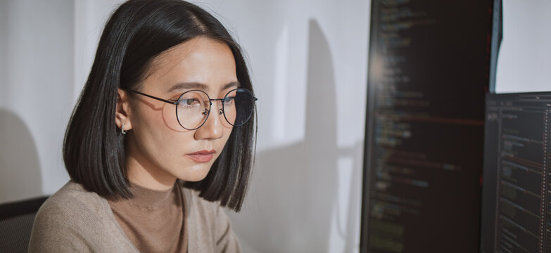 Young adult Asian female software developer coding program on desktop computer. Woman work from home, remote working, freelance programmer job, smart digital nomad lifestyle concept