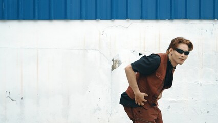 Handsome street dancer practicing break dancing at white back ground. Sport man wearing hip hop style while moving footsteps to music at street with blue background. Outdoor sport 2024. Hiphop.