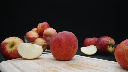 Macrography of apples displayed in various forms: whole, sliced, and within a glass bowl with black background. Each close-up shot captures the red colors of the apples on cutting board. Comestible.