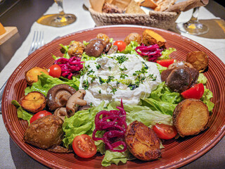 Ensalada colorida con diversos ingredientes, incluyendo champiñones, papas, tomates y una crema en el centro.