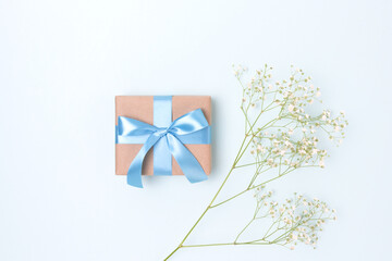 Gift box with a tied ribbon and branch of gypsophila flower on a blue background.