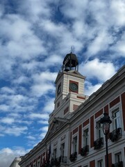 The iconic clock tower of Puerta del Sol, Madrid, against a dramatic sky of scattered clouds, showcasing the heart of Spain's capital and its vibrant history and culture in a single frame.