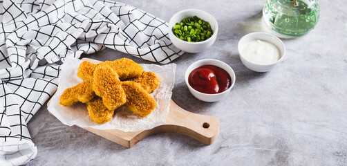 Crispy nuggets on paper on a board and sauce in a bowl on the table web banner