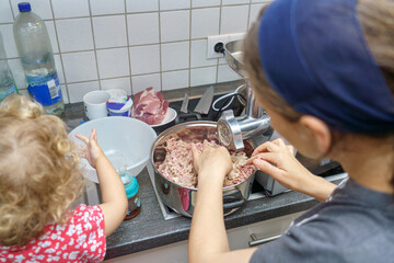 Mom makes minced meat and her little daughter helps her in the kitchen.