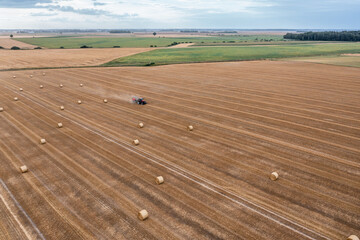 Obraz premium Aerial view of a agro-cultural field after harvesting and baler presses straw into bales