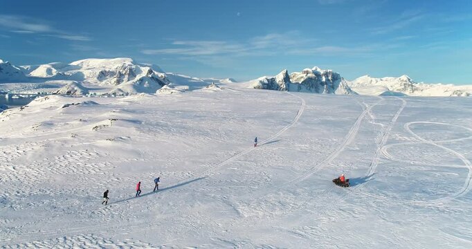People enjoy outdoor sport activity in Antarctica. Group of scientists from polar station run snow trail race. Travel, active lifestyle, recreation in arctic wild nature landscape. Aerial drone shot