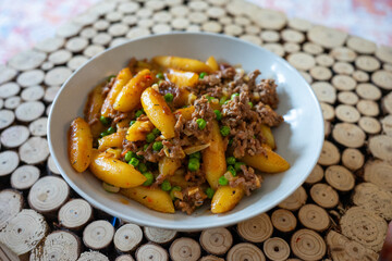Plate of gnocchi with minced meat and green peas served on a patterned placemat.