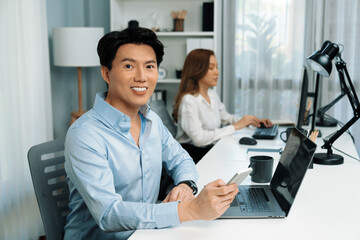 Profile smart Asian businessman looking camera to pose using smartphone at modern office. Blurry...