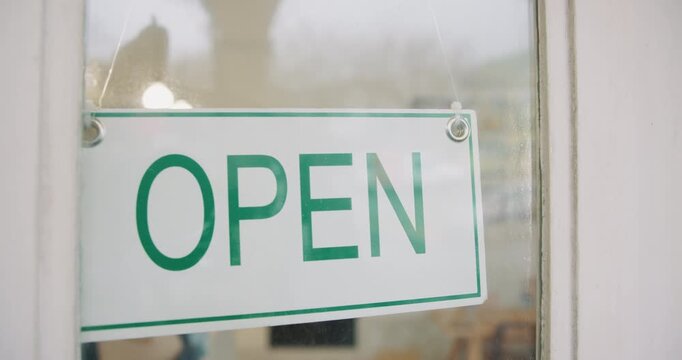 Door, hands and open sign in cafe for small business as notice or notification for customers. Person, owner or waitress in window at coffee shop or restaurant in startup for operating and trading