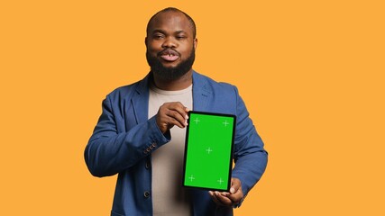 Portrait of african american man doing influencer marketing using green screen tablet, studio background. Smiling BIPOC person holding empty copy space mockup device, camera A