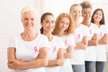 Obraz premium Breast Cancer Campaign. Multiracial Women In Pink T-Shirts With Awareness Ribbons Standing In Line Over White Background. Shallow Depth