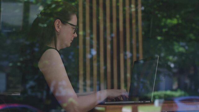 Female freelancer sits in cafe working in laptop view from street through window. Freelancer worker flexibility and freedom of modern freelancing work can be done from anywhere Freelancer works
