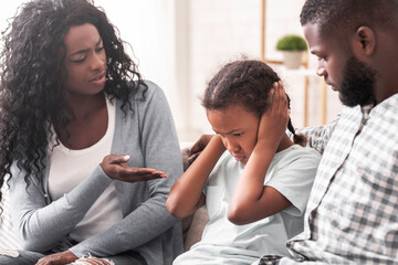 Family education. Little black girl closing her ears not to listen parents scolding