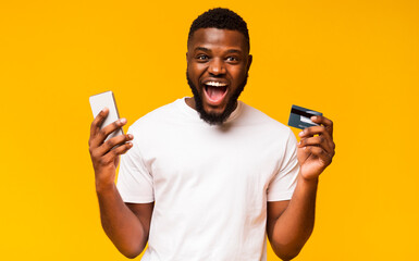 Easy payments. Happy african man holding credit card and smartphone in his hands, free space