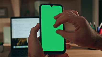 Freelancer hand zooming greenscreen mobile phone at evening home close up.