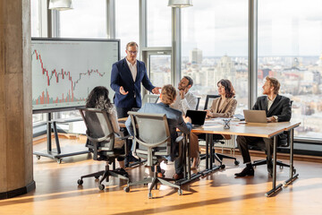 A group of business professionals are gathered around a table in a modern office, analyzing a...
