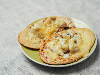 Meal with two pita bread with chopped cooked chicken fillet and melted cheese on a green plate and light color table clothes. Pizza style dish. Quick lunch.