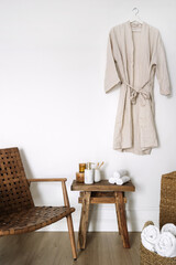 Bathrobe hanging on wall over bench with dispenser bottle, toothbrush in holder cup, towels, chair...