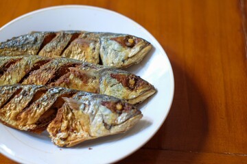 Fried mackerel in a white plate on a wooden table, healthy seafood concept, copy space.
