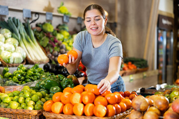 Young woman chooses tangerines for purchase in greengrocer shop