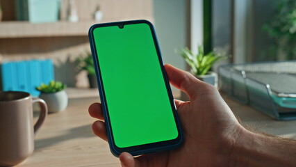 Smartphone user looking green screen display at office desk close up. Man hand 