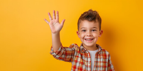 Cheerful boy waving hand and smiling on yellow background