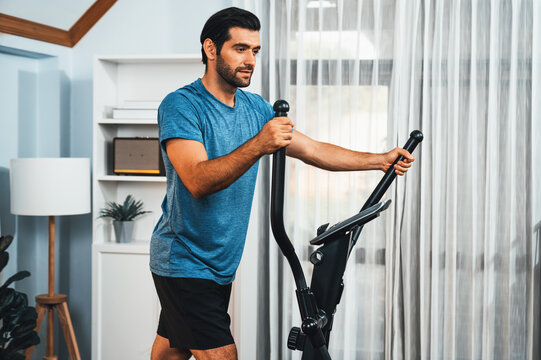 Athletic and sporty man running on elliptical running machine during home body workout exercise session for fit physique and healthy sport lifestyle at home. Gaiety home exercise workout training.