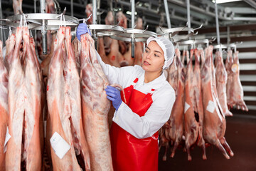 Fototapeta premium Female butcher looking at mutton carcass in meat storage