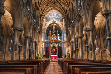 Fototapeta premium Grand church interior in Cambridge, UK, featuring high vaulted ceilings, wooden pews, a golden rood screen, and colorful stained glass windows.
