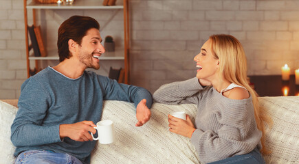 Happy Couple Spending Time Together Drinking Tea And Talking Sitting On Sofa At Home. Selective Focus