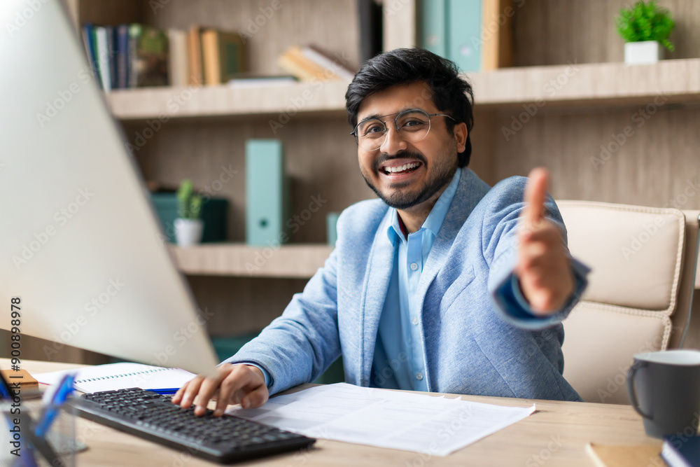 Aufkleber indian businessman in a blue suit smiles and gives a thumbs up while sitting at his desk and working