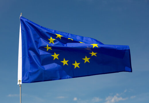 Huge flag of EU attached on long handle against background of clear bright sky