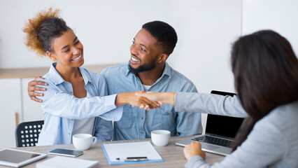Obraz premium Budget planning. Positive afro couple handshaking with investment counselor in office. Selective focus