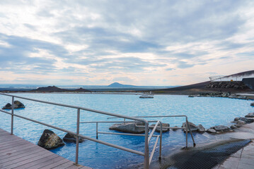 Experience the tranquility of Myvatn Nature Baths in Iceland, featuring a blue geothermal pool, wooden deck, and stunning views of rolling hills and distant mountains.