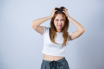 Fototapeta premium Frustrated woman pulling her hair, expressing stress and anxiety, wearing casual clothes and standing against a white background.