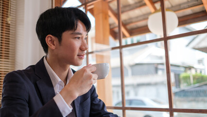 Portrait of smiling businessman in suit enjoying morning coffee while sitting at working desk with laptop.