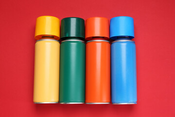 Many spray paint cans on red background, top view