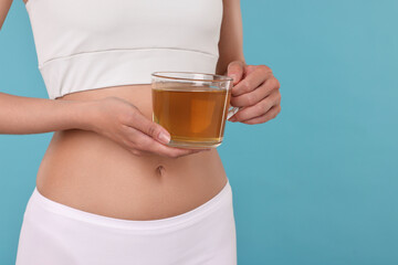 Weight loss concept. Woman with cup of diet tea on light blue background, closeup