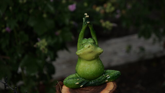 A frog statue is sitting on a log, with its hands in a prayer position