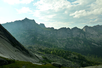 Fototapeta premium A view from the top of a gentle mountain at the spiky rocks of a mountain range running like a rocky chain under a cloudy summer sky.