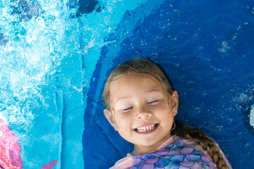 Portrait of a cute Caucasian little girl in a pool. Happy smiling child with eyes shut in water....