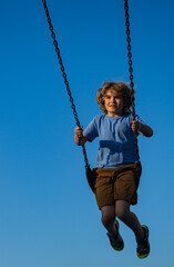 Kid on chain swing, having fun against blue sky. Carefree and freedom childhood. Active kid playing outdoors. Child at playground. Cute kid having fun on a playground outdoors in summer. Kid swinging.