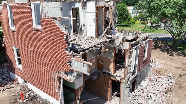 Excavator demolishing house. Ground level demolition with debris falling. Aerial of condemned home being torn down. Sunny day in american suburb. Destroyed house wall.-