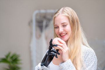 A young woman is using a robotic prosthetic arm attached to her body. She controls her hand to pick...